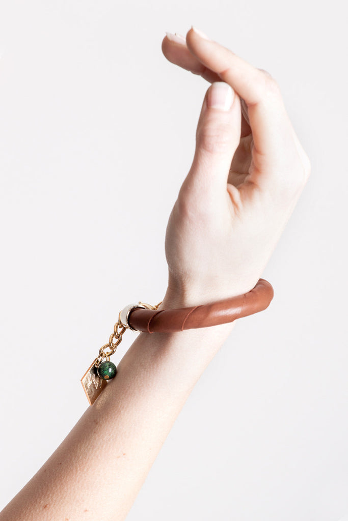 The no. 13 edition of the handcuff bracelet is made of cognac brown leather with galvanized metal components and aventurine.
