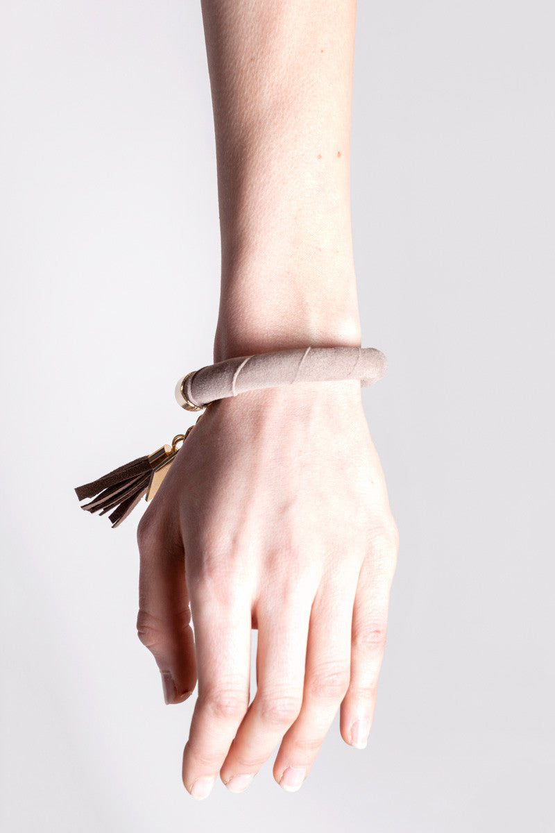 The no. 5 edition of the handcuff bracelet is made of beige suede with galvanized metal components with leather tassel. Gold edition.