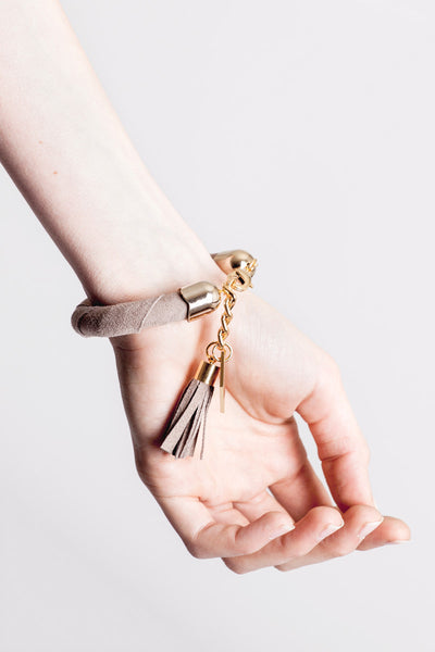 The no. 5 edition of the handcuff bracelet is made of beige suede with galvanized metal components with leather tassel. Gold edition.